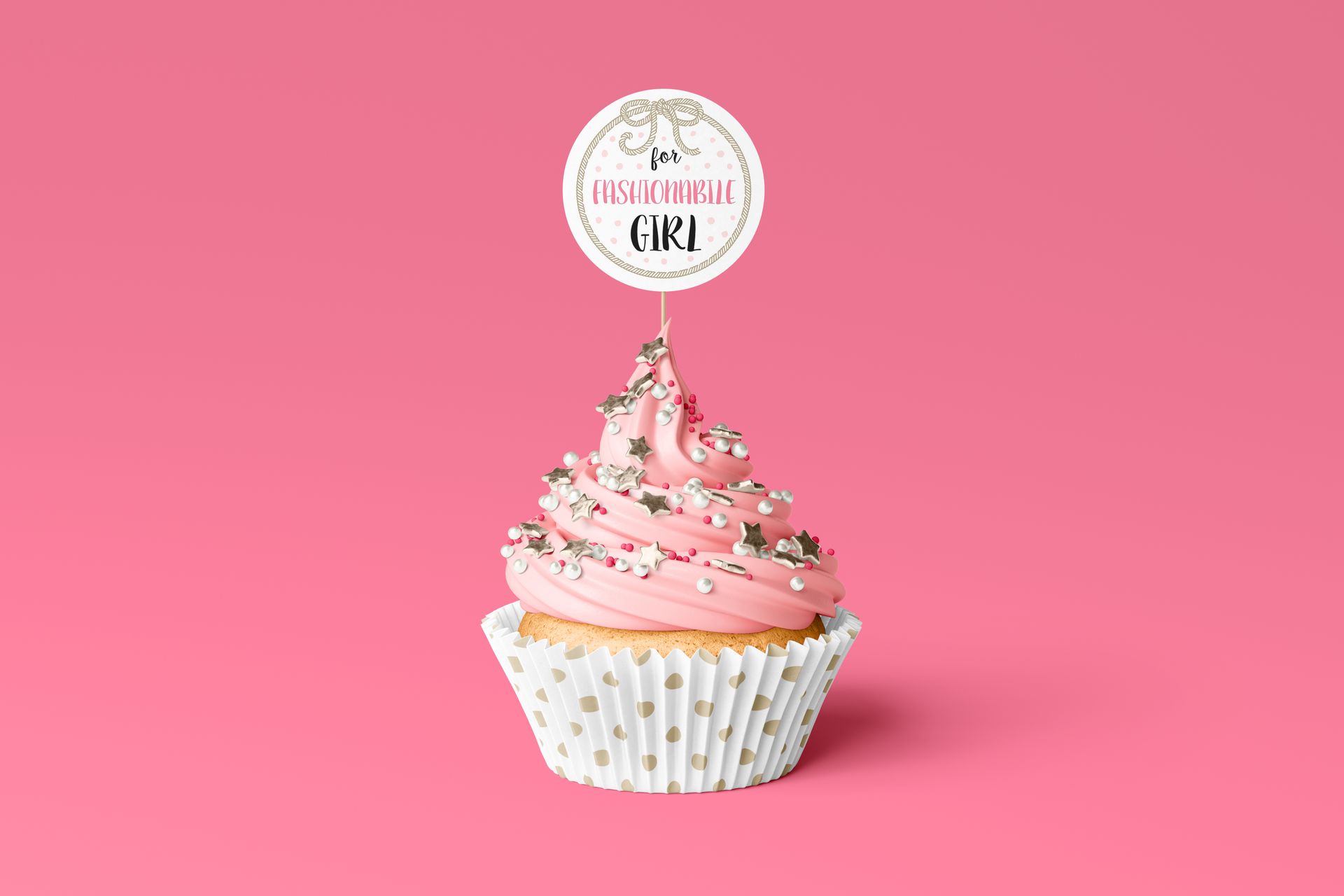 Single cupcake with pink frosting, white sprinkles, and a round topper displayed on a pink background, mockup style.