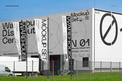 Front view of a modern warehouse distribution center with large mockup banners and signage, surrounded by a metal fence and green grass.
