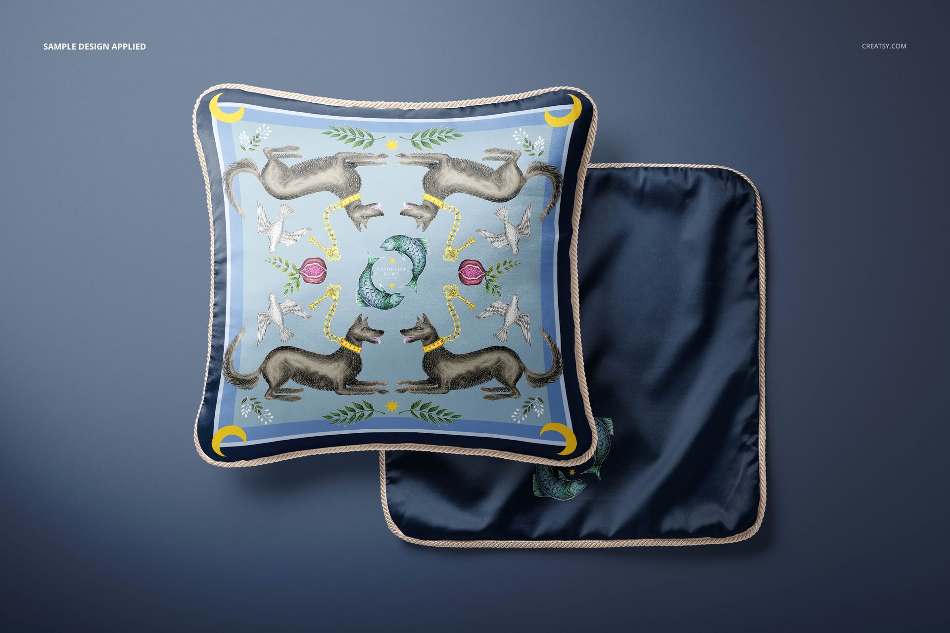 Silk cushion mockup set with braided trim, displaying a colorful animal motif and navy back on a blue surface.