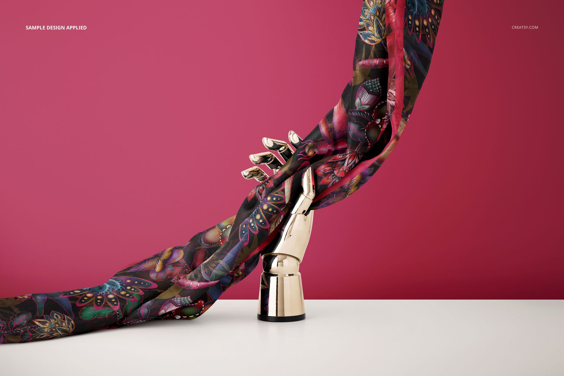 PSD mockup of a patterned habotai silk scarf wrapped around a shiny mannequin hand, set in front of a pink wall.