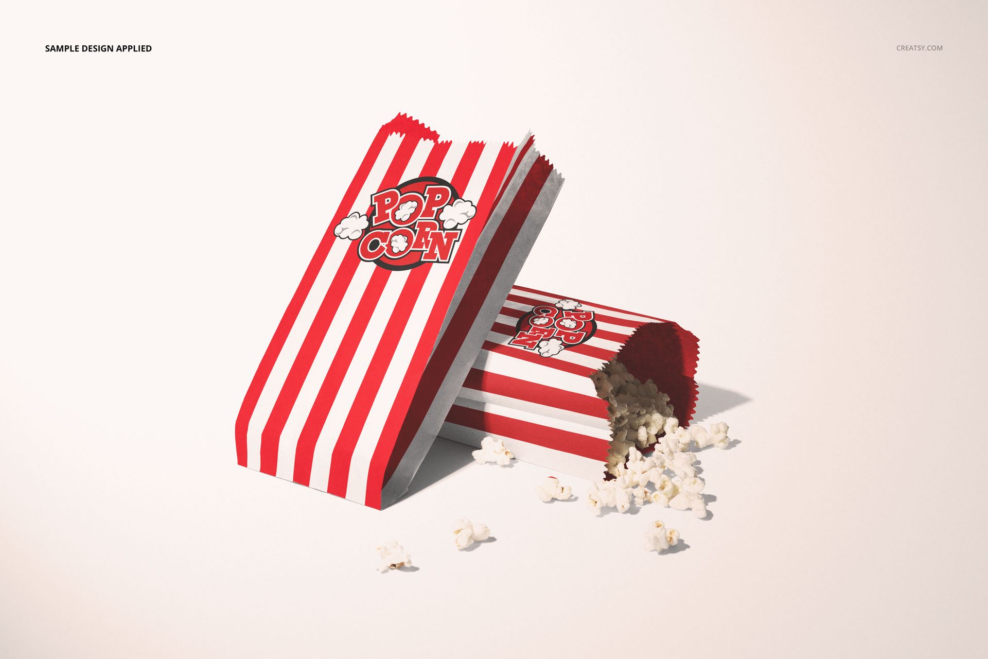 Popcorn paper bag mockup featuring vertical red and white stripes, with popcorn scattered beside the bags on a light surface.
