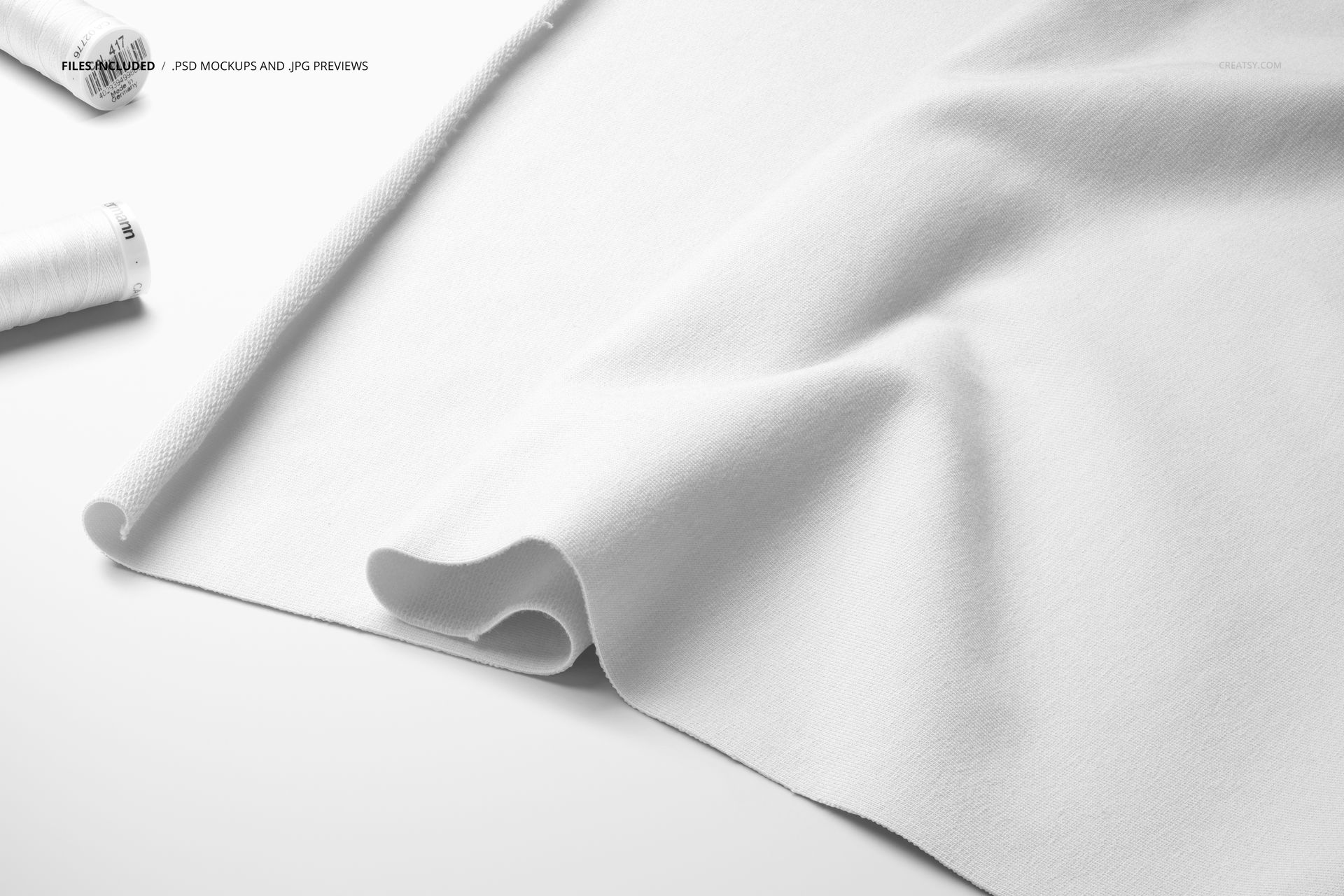 Draped white jersey fabric mockup displayed on a flat surface with two white thread spools in the corner.