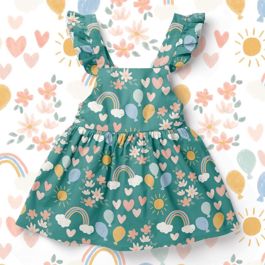 Baby dress mockup displayed from the front, featuring a colorful pattern with rainbows, balloons, hearts, and flowers on a teal background.