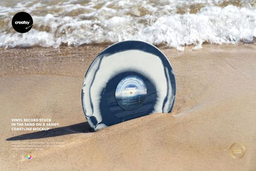 PSD mockup showing a vinyl record embedded in light brown sand at the edge of a beach, waves rolling in behind.