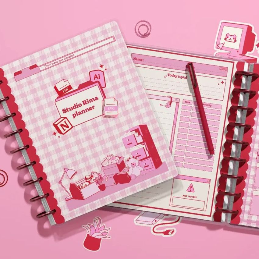 Pink-themed spiral planner mockup seen from above, featuring illustrated covers, an open page, and minimal office props.