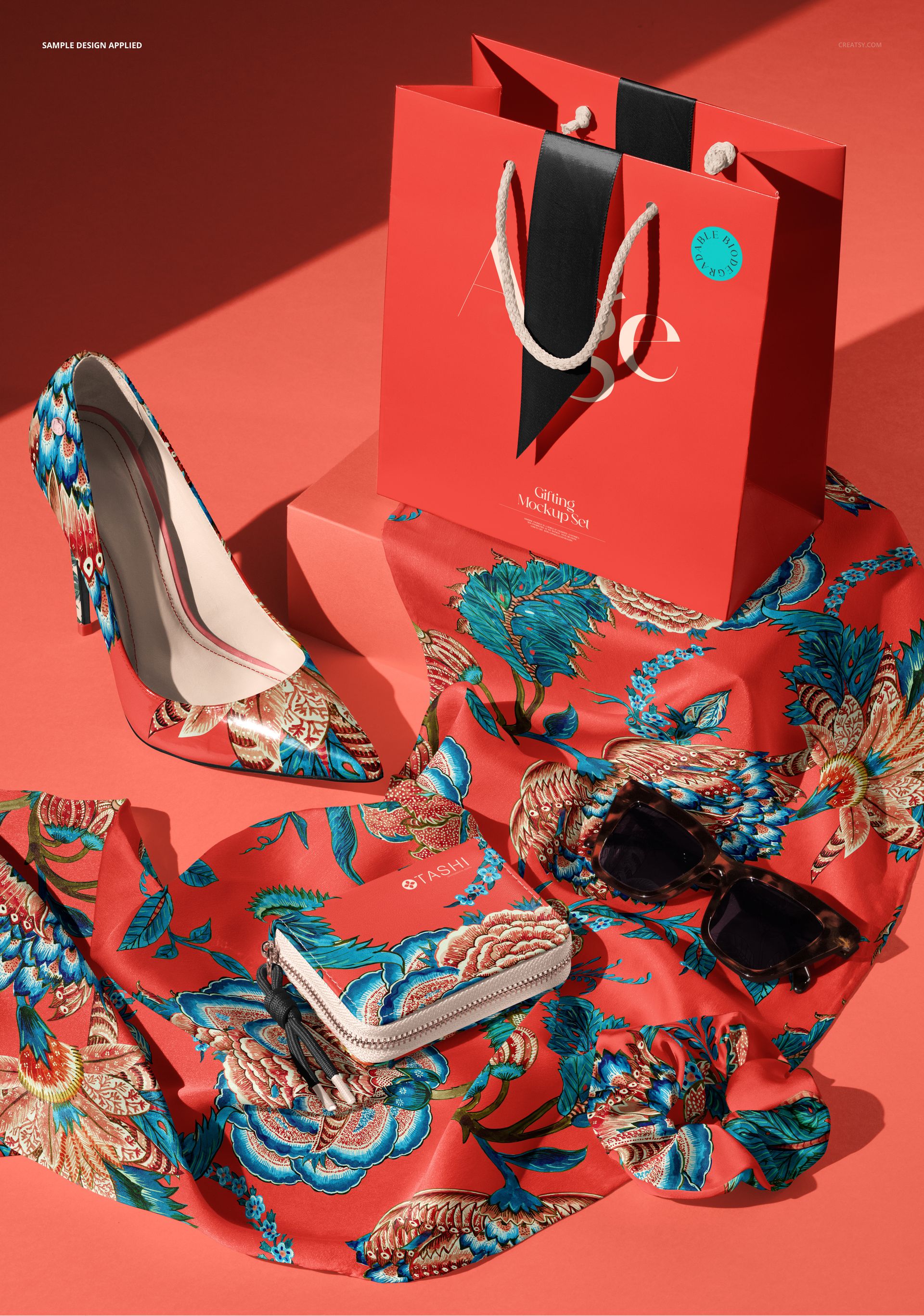 Top view of a mockup scene with patterned silk scarf, matching scrunchie, high heels, wallet, sunglasses, and red gift bag.