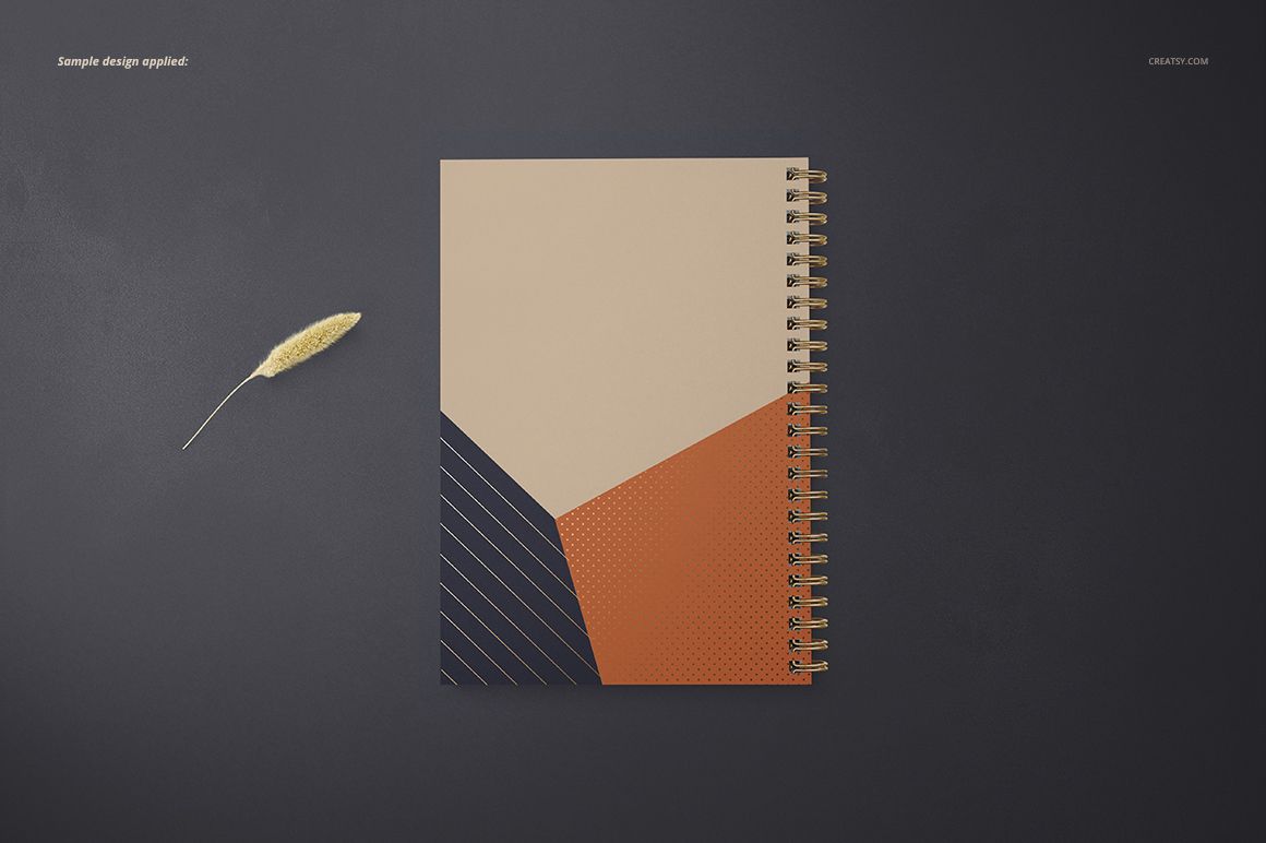 Top view of A5 spiral notebook mockup with square holes, beige and orange geometric cover, on dark surface.