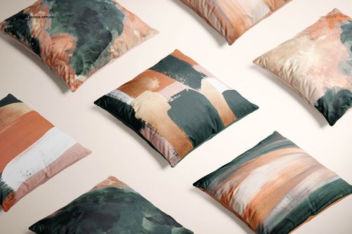 PSD mockup of cushion covers with painterly abstract patterns in dark green, peach, and cream, scattered on a pale background.