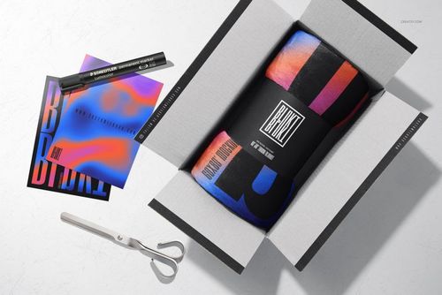 Rolled fleece blanket mockup in a cardboard box, featuring a vibrant design with blue, red, and black accents.