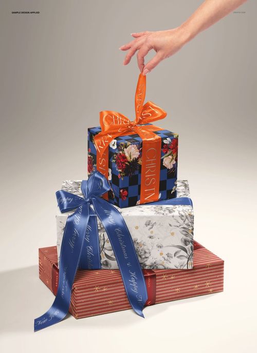 PSD mockup of three gift boxes in different festive designs and colors, viewed from the front with a hand reaching for the top ribbon.