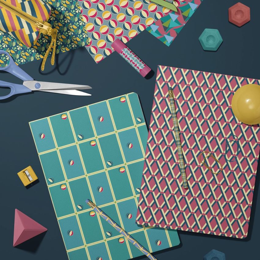 Stationery mockup featuring two classic A4 notebooks with bold geometric covers, surrounded by colorful office supplies on a dark surface.