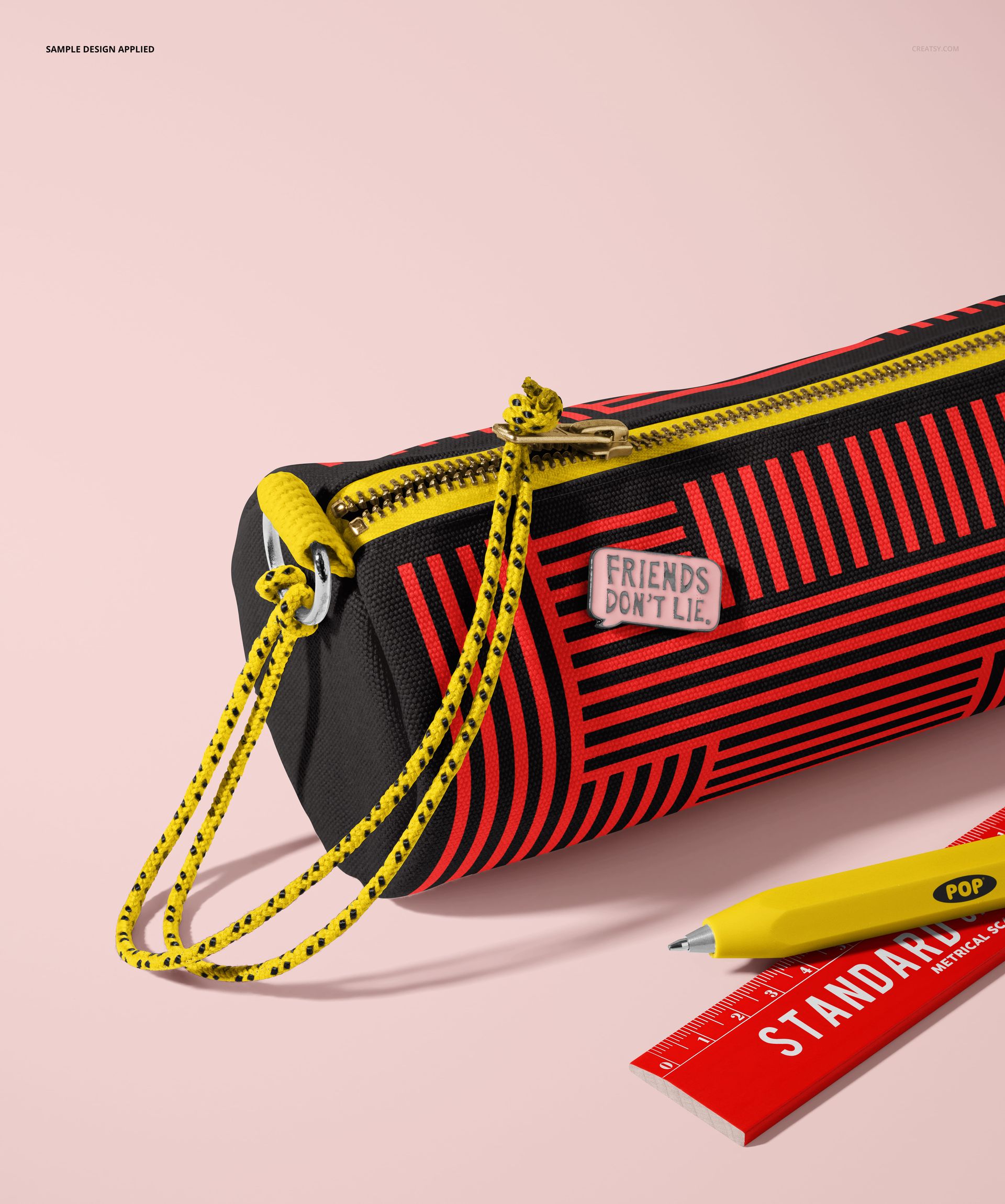 Fabric pencil case mockup with red geometric stripes, yellow zipper, and two pencils on a light pink surface.