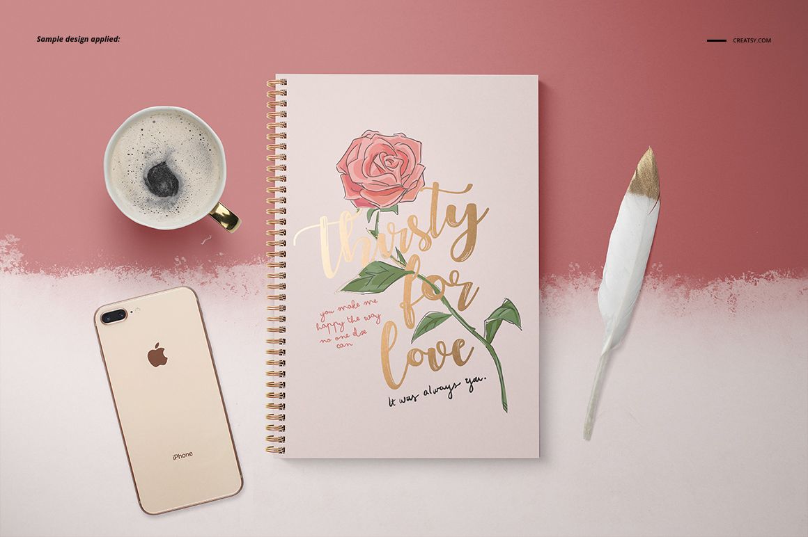 Front view of an A4 notebook mockup with spiral binding, rose artwork, and gold text, next to coffee, phone, and brush.