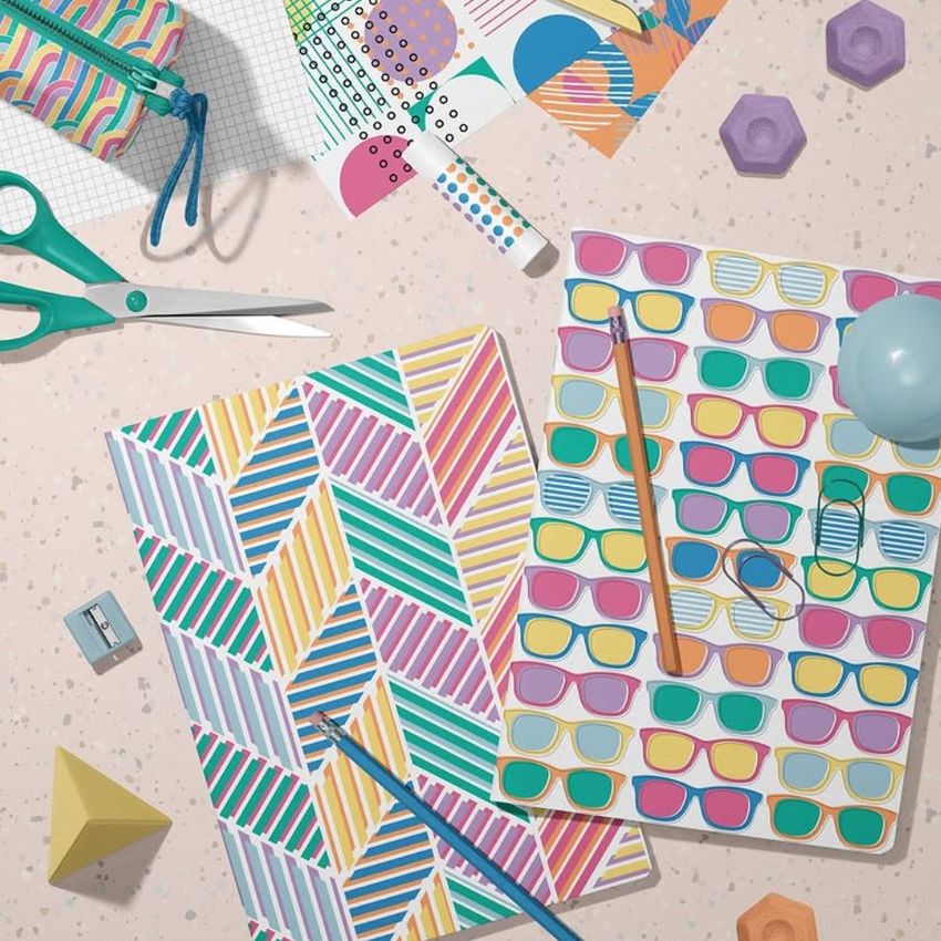 Stationery mockup featuring two classic A4 notebooks with colorful geometric and sunglasses patterns on a speckled surface.