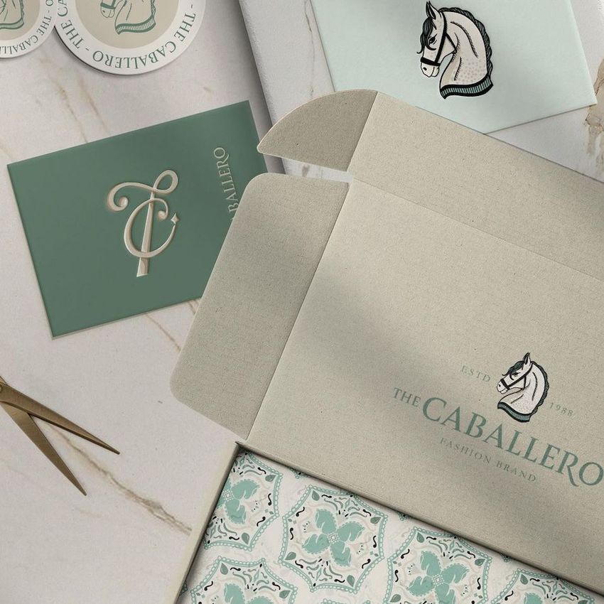 Mailing box mockup featuring an open cardboard box with patterned tissue paper, green cards, and a round sticker on a marble surface.