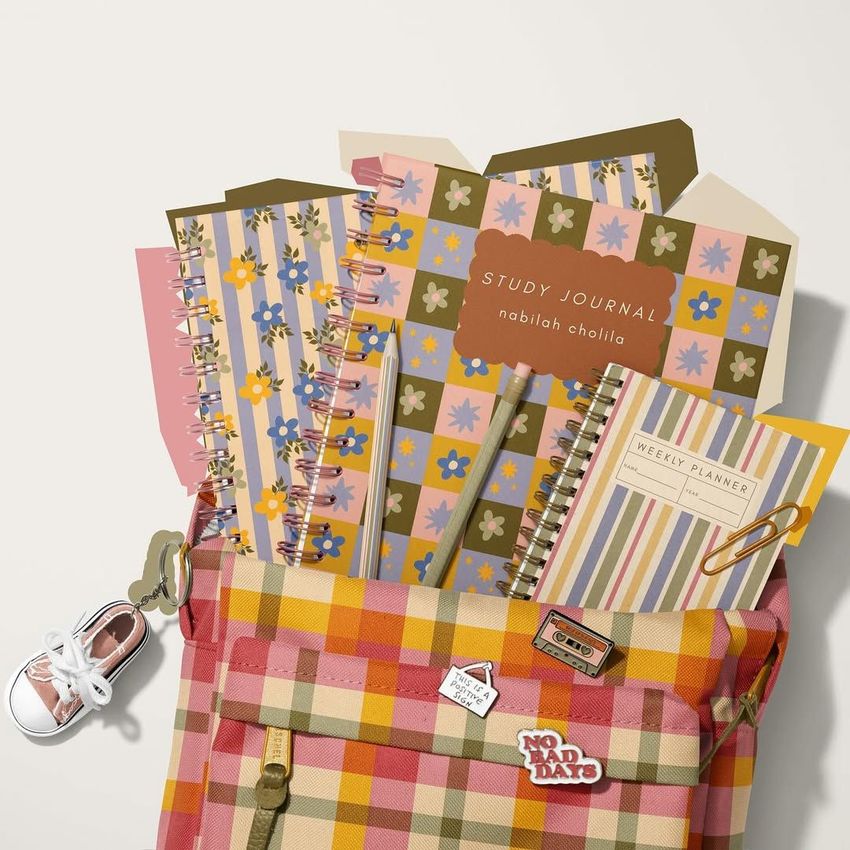 School backpack mockup with a plaid pattern, filled with spiral notebooks featuring colorful floral and geometric covers, shot from above.