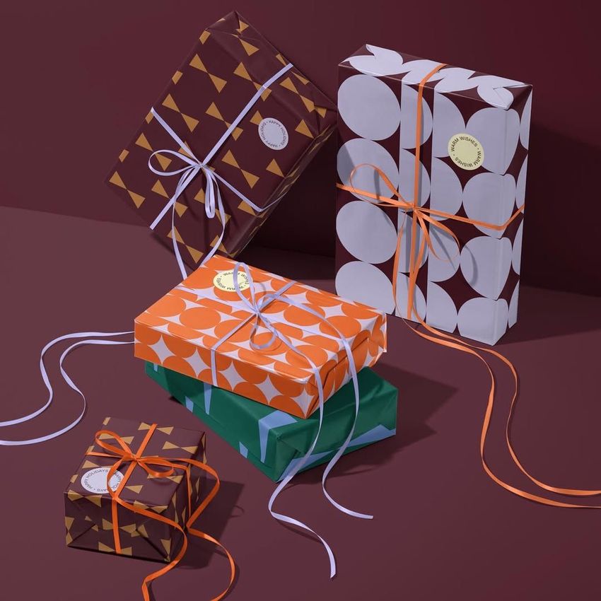 Christmas gifts wrapping mockup featuring five boxes with geometric patterned paper in brown, orange, and green tones, tied with ribbons.