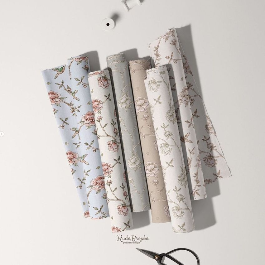 Fabric rolls mockup featuring six patterned textiles with floral and bird motifs, arranged on a light surface with sewing props.