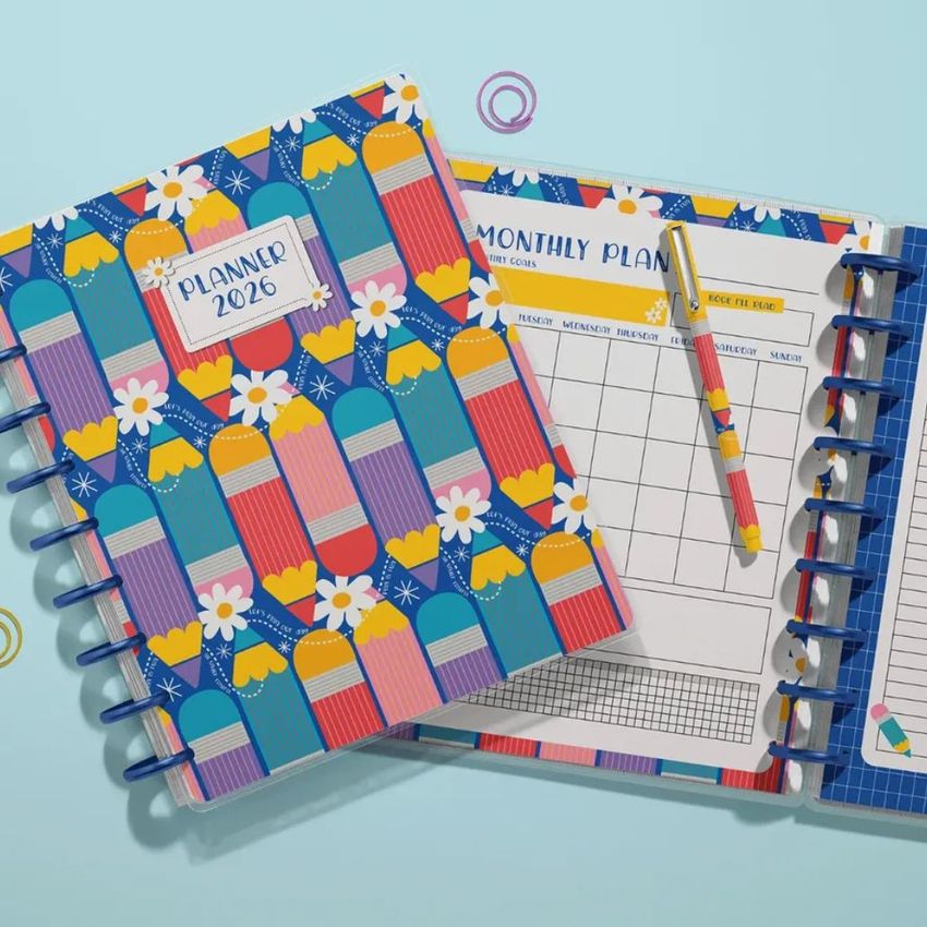 Top view of two spiral planners with colorful pencil and daisy patterns on the covers, shown on a light blue background with a pencil and geometric props.