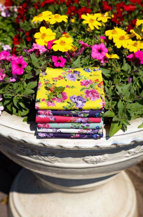 PSD mockup showing multiple folded fabric pieces with bright floral designs set on a large flower-filled planter.