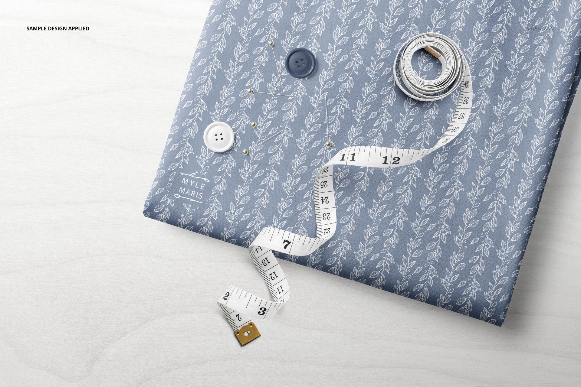 Folded textile mockup featuring a blue leafy design, accompanied by white and gray buttons and a tape measure.