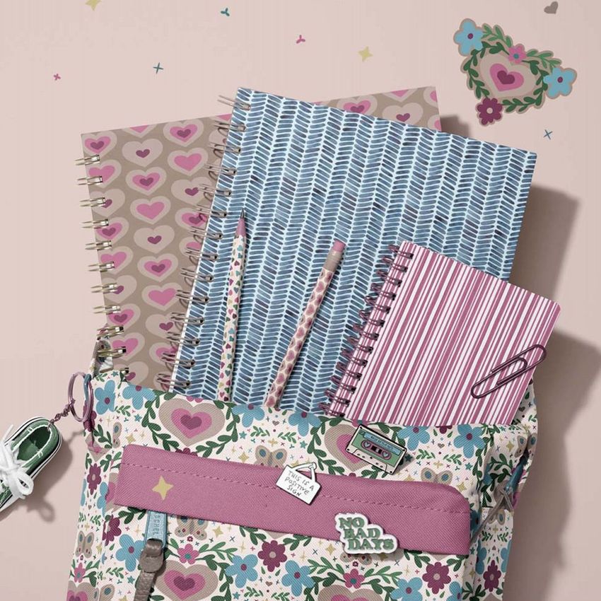 School backpack mockup with floral pattern, holding three spiral notebooks in pastel colors and two patterned pens on a light surface.