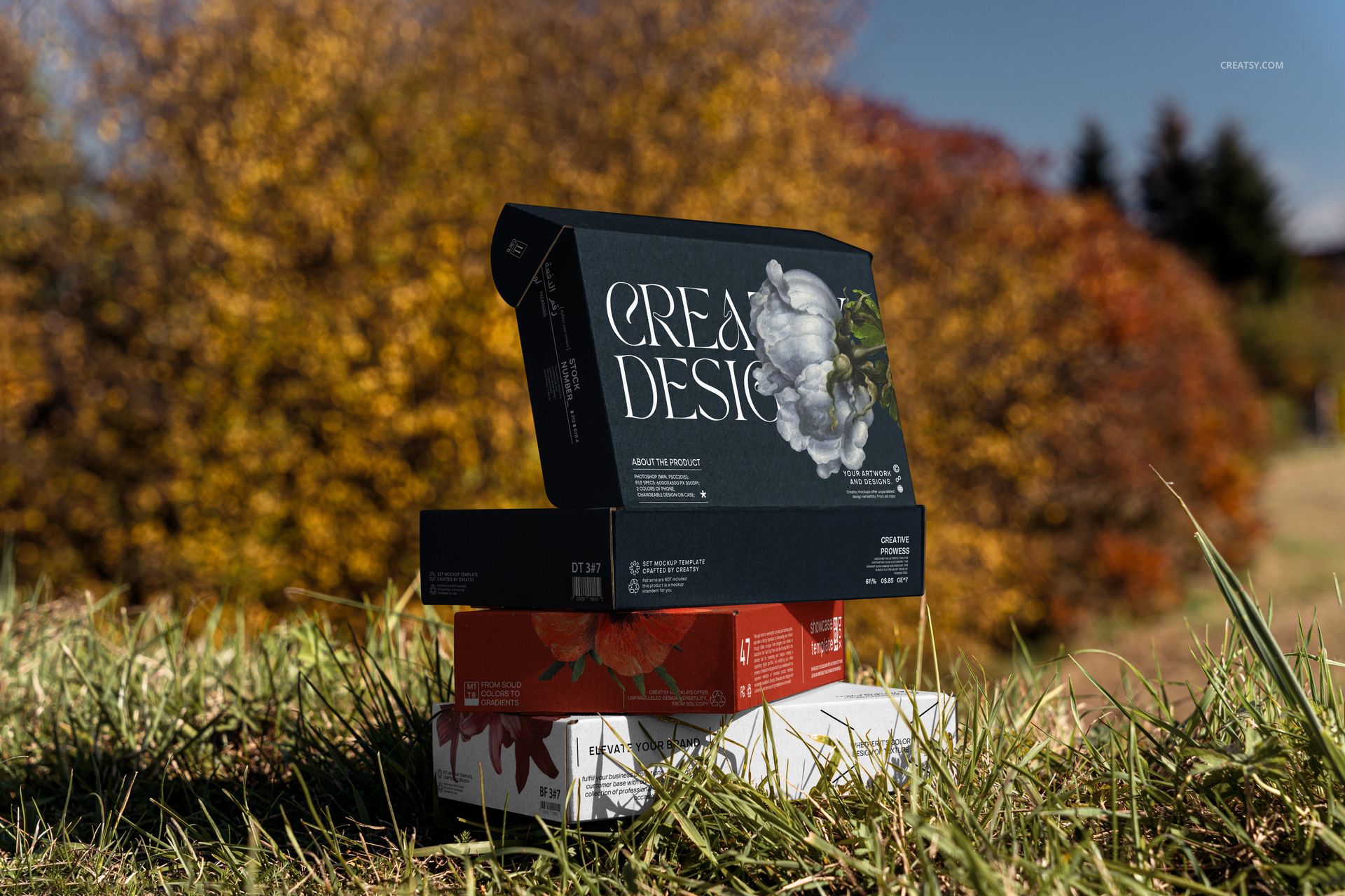 PSD mockup showing a pile of packaging boxes with creative graphics set on grassy ground, autumn landscape visible.