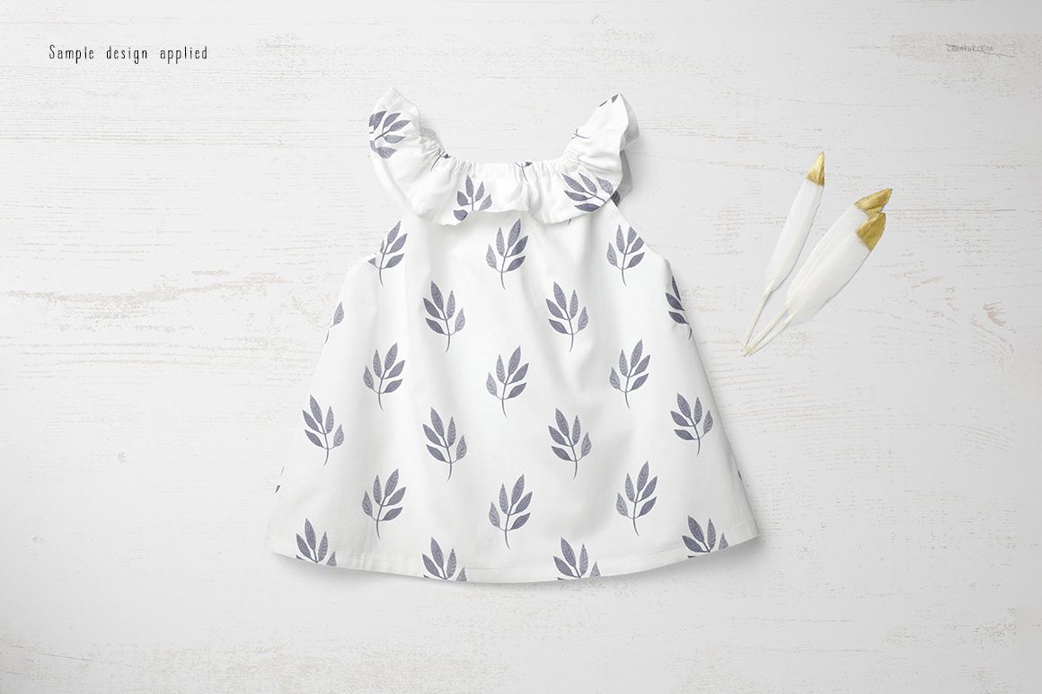 Front view of a baby summer dress mockup with a white fabric and gray leaf pattern, displayed on a light wooden surface.
