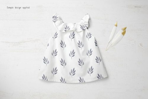 Front view of a baby summer dress mockup with a white fabric and gray leaf pattern, displayed on a light wooden surface.