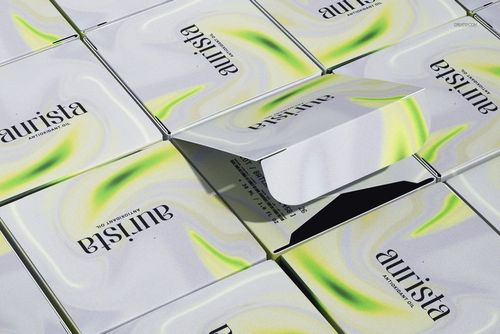 Several square cosmetic boxes with a green and yellow swirl pattern are arranged in a grid, one box partially opened.