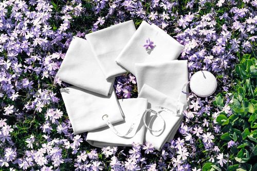PSD mockup showing several white fabric swatches placed in a circle on a vibrant floral background outdoors.