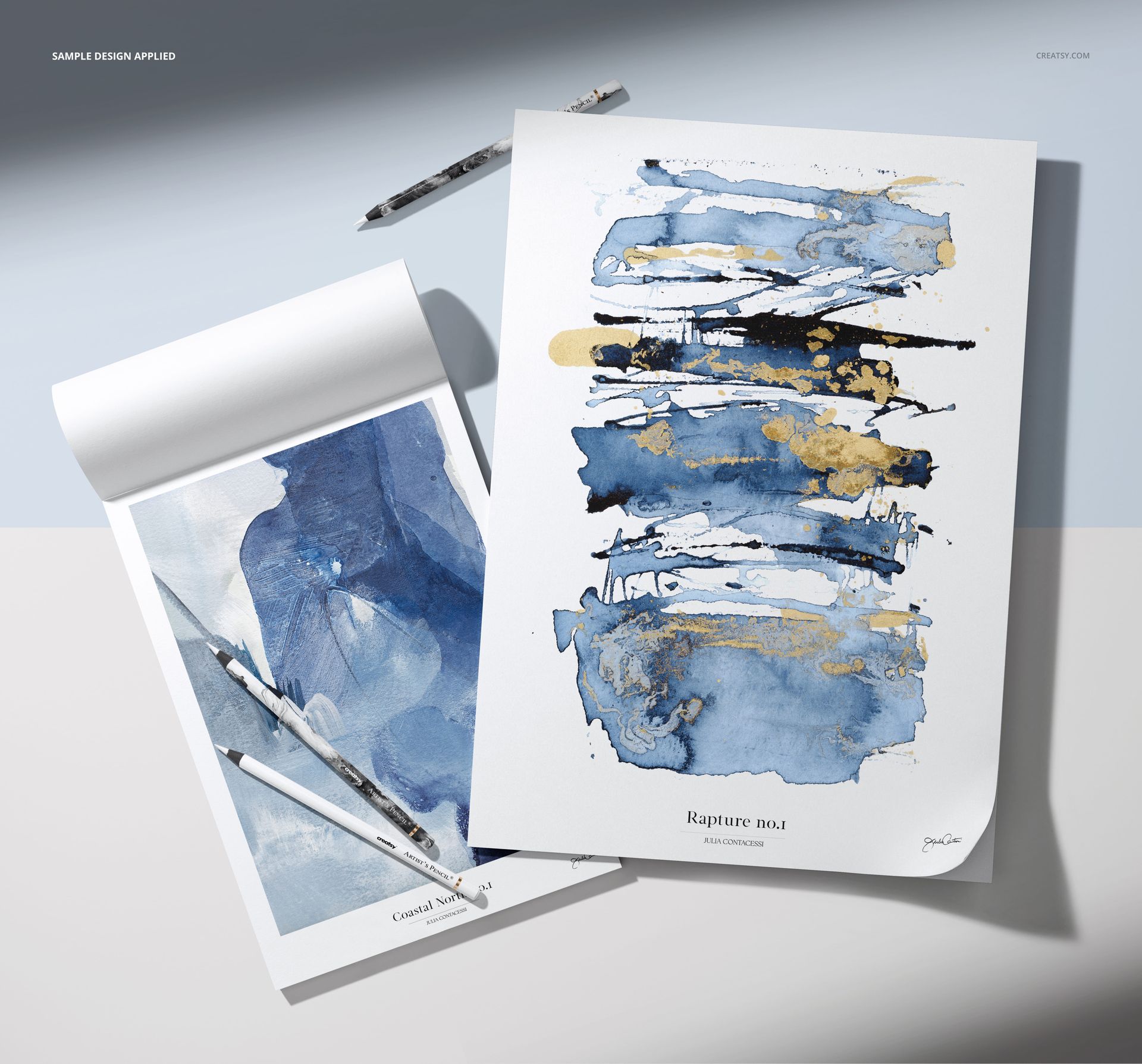 PSD mockup showing two decorative drawing pads with abstract watercolor artwork and pencils on a light surface.