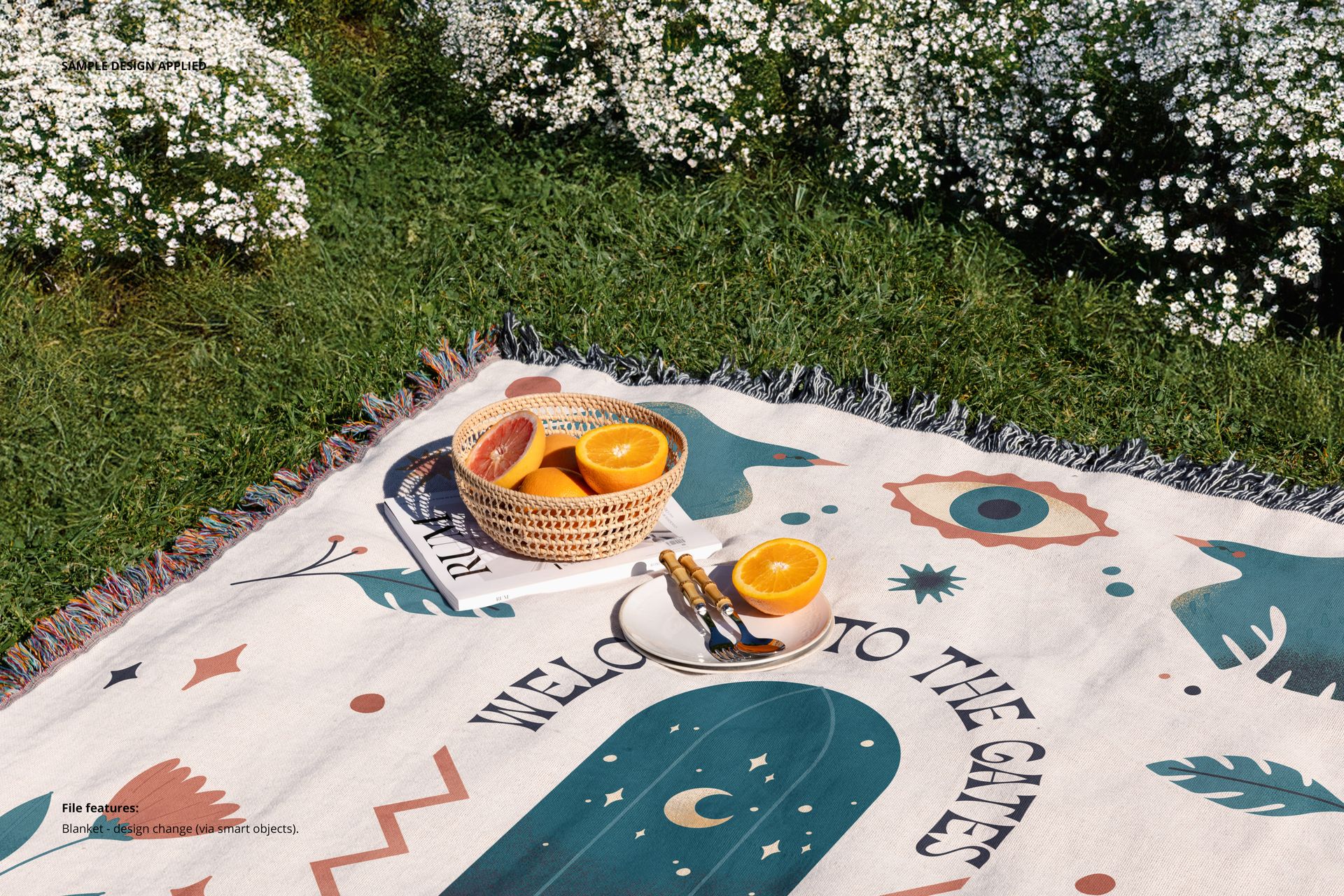 Woven blanket mockup with multicolor fringe, basket of oranges, and book arranged outdoors beside blooming plants.