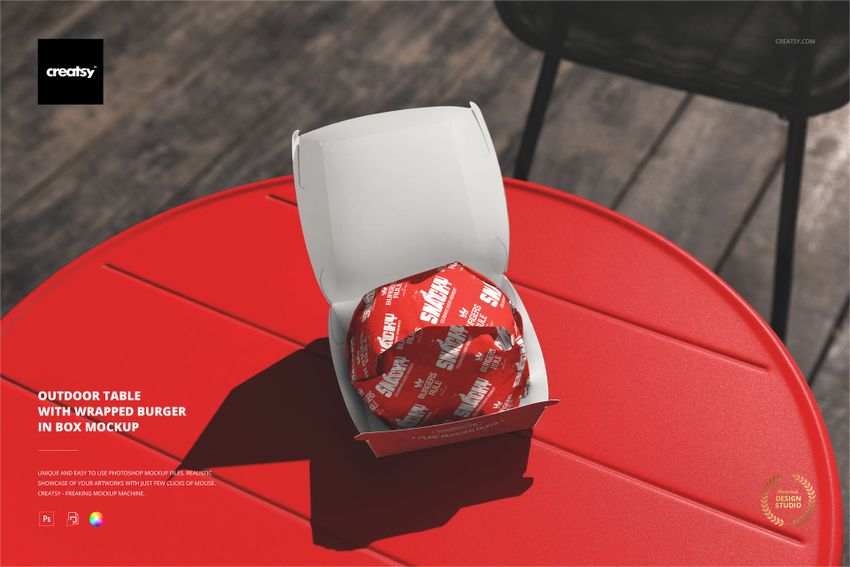 Top view of a mockup featuring a wrapped burger in a white box placed on a bright red circular table outdoors.