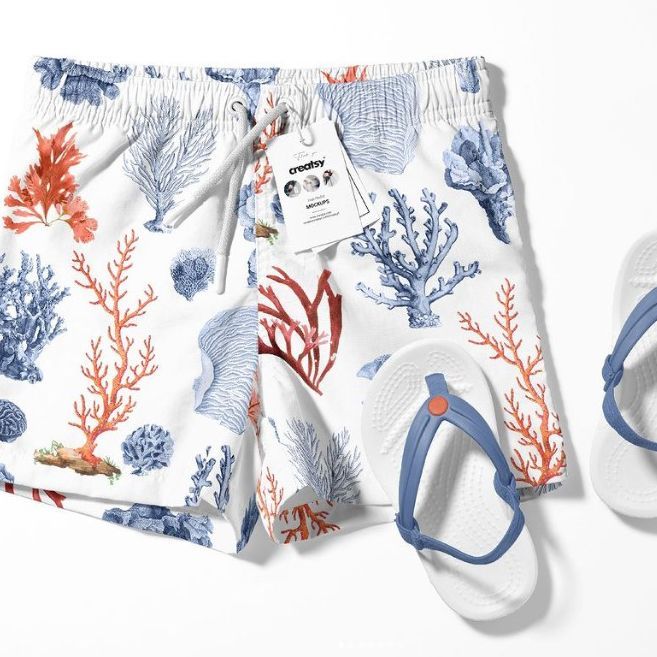 Kids swim shorts mockup featuring a coral reef pattern in blue, red, and orange, shown with white flip-flops on a white background.
