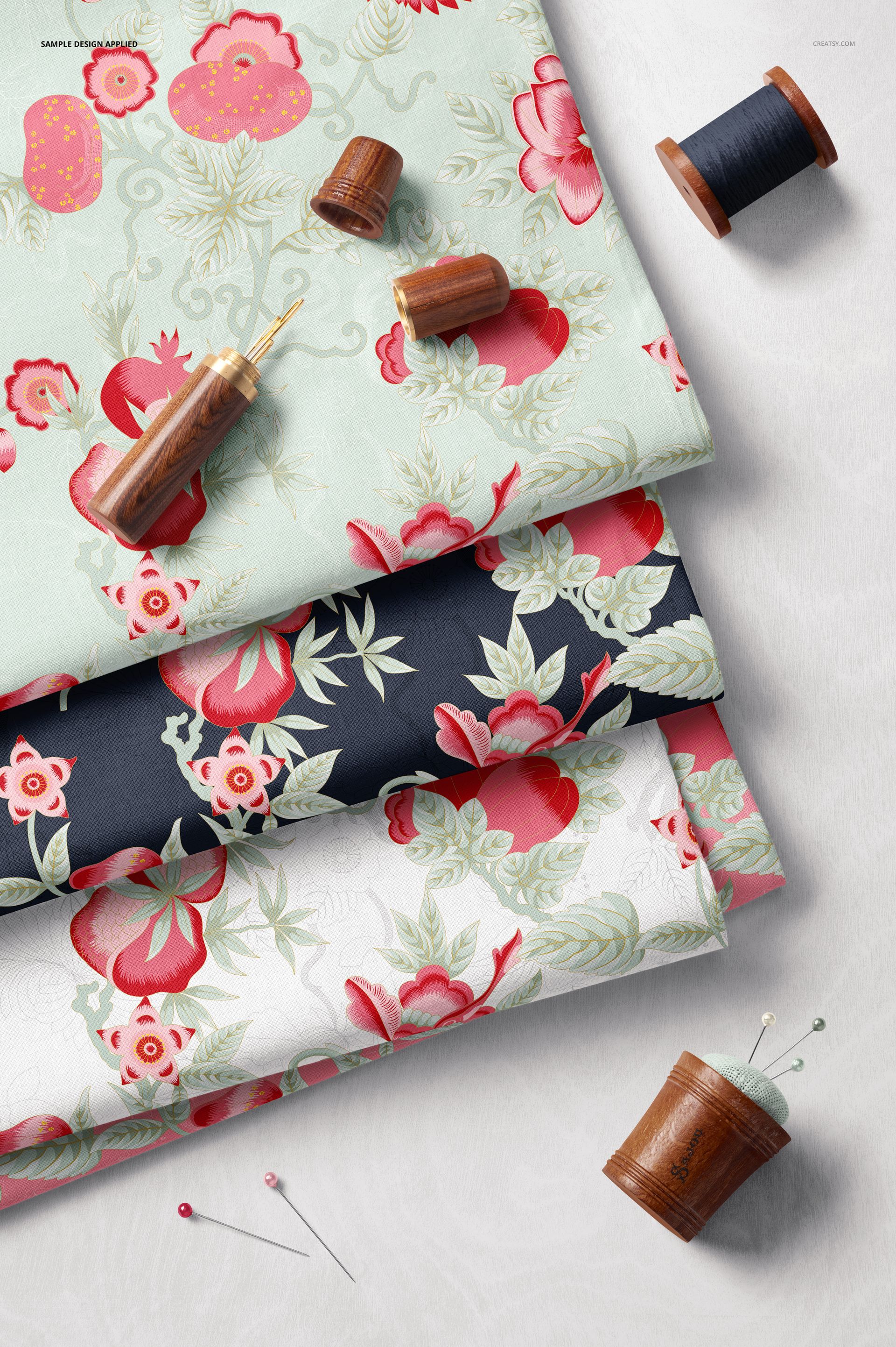 PSD mockup showing layered cotton fabrics in different colors and floral prints, accompanied by spools and pins.