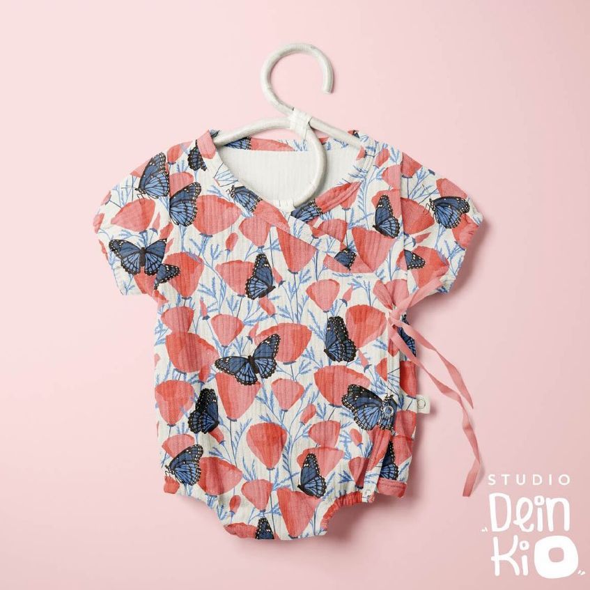 Muslin onesie mockup featuring a short-sleeve baby bodysuit with a butterfly and poppy pattern, displayed on a hanger against a light pink background.