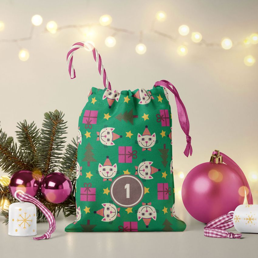 Drawstring sacks advent calendar mockup featuring a green bag with cat and present patterns, set with pink ornaments and fairy lights.
