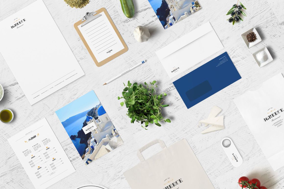 Greek restaurant branding mockup with stationery, menu, envelopes, and food props arranged on a white wooden surface.