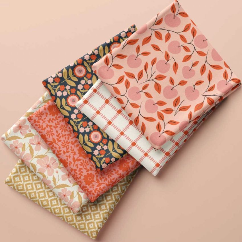 Folded fabrics mockup featuring five stacked textiles with various floral, fruit, and geometric patterns in warm tones.