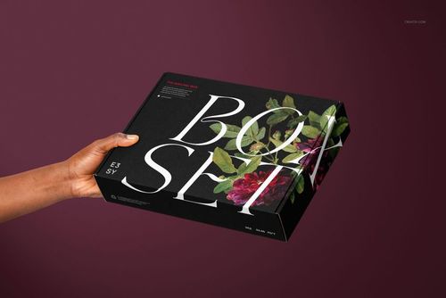 PSD mockup of a mailing box featuring floral graphics and oversized white text, presented in a person's hand.