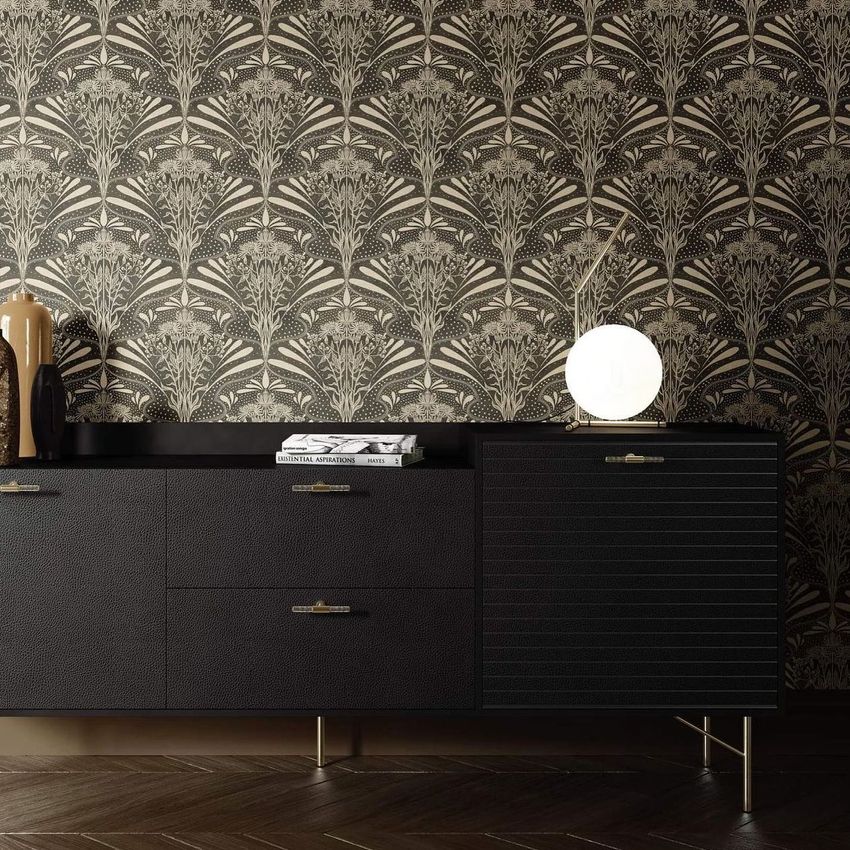 Interior wallpaper mockup showing a black and gold botanical pattern behind a modern black sideboard with a round lamp.