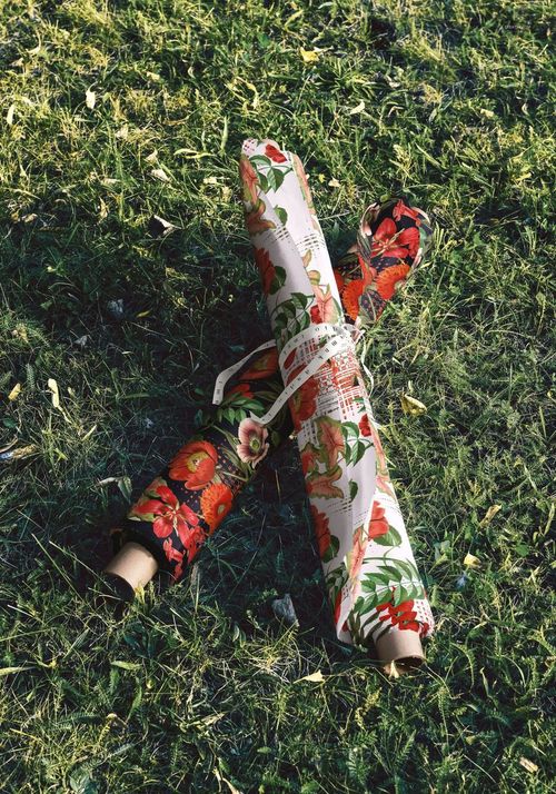 PSD mockup of stacked fabric rolls with red and green floral prints placed outdoors on a grassy surface.