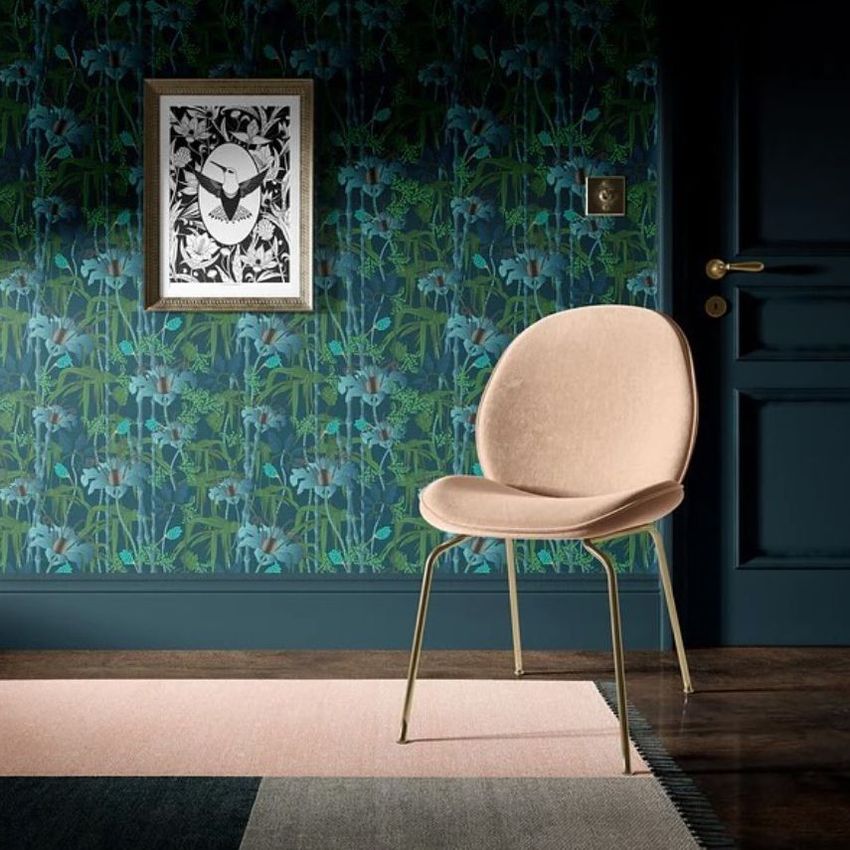Interior scene mockup showing a beige chair with gold legs in front of a dark floral wallpaper and framed artwork.