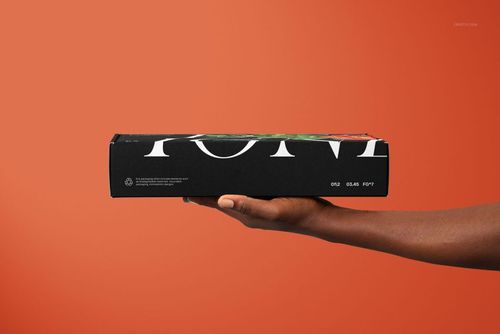 Black mailing box mockup featuring large white lettering, displayed horizontally in a hand with an orange backdrop.