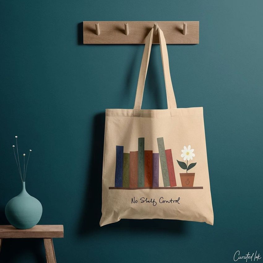 Tote bag mockup hanging on a wooden hook rack against a teal wall, featuring a bookshelf and potted flower graphic design.
