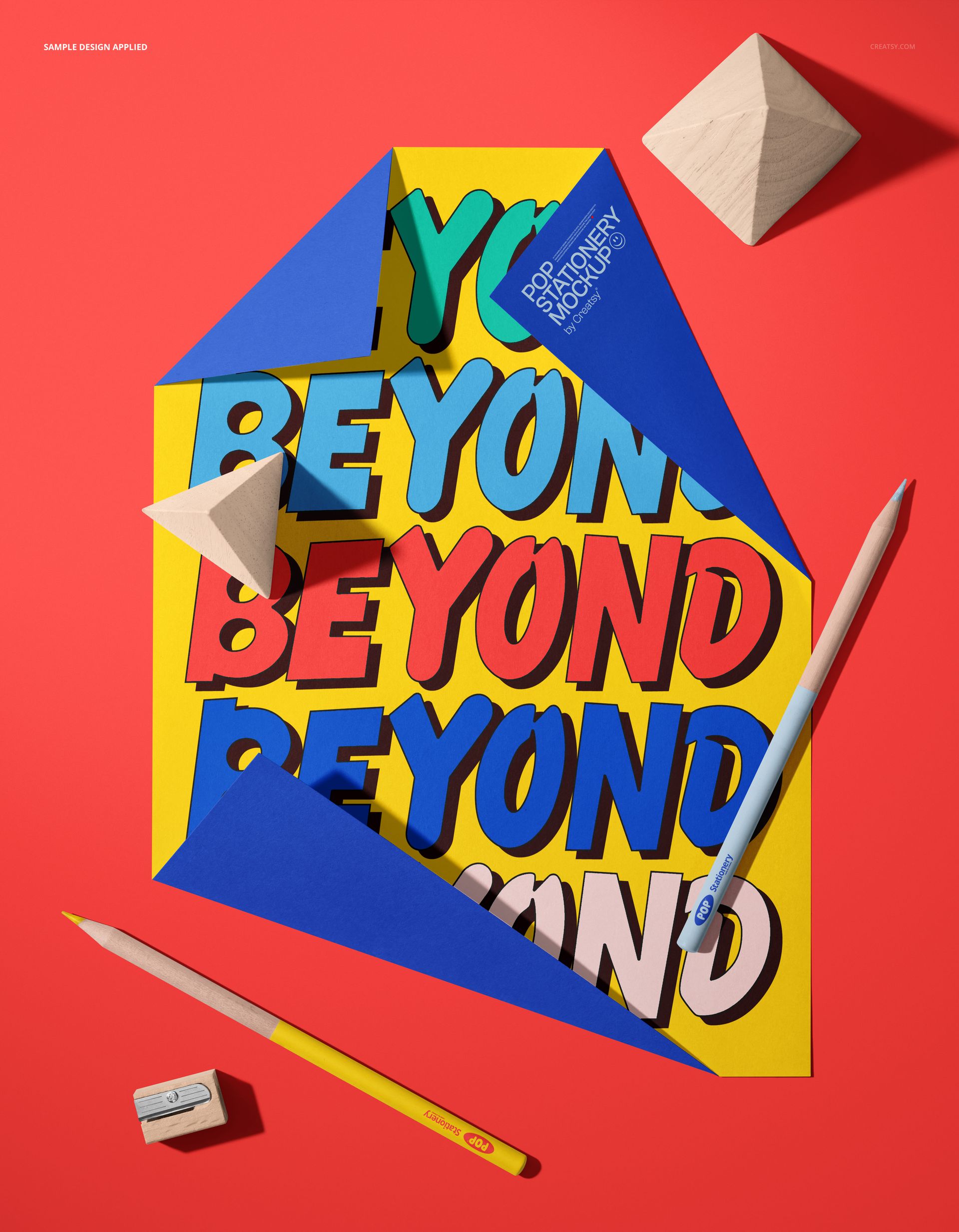 Stationery mockup featuring a colorful poster with folded blue corners, crayons, pencils, and wooden geometric props on a red background.