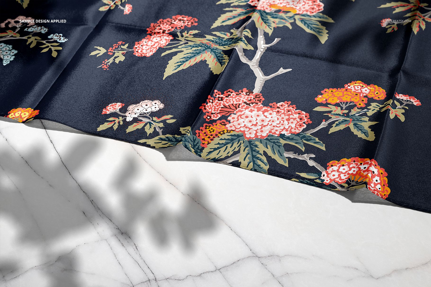 Elegant silk scarf mockup featuring colorful flowers and leaves on dark fabric, laid out on white marble.
