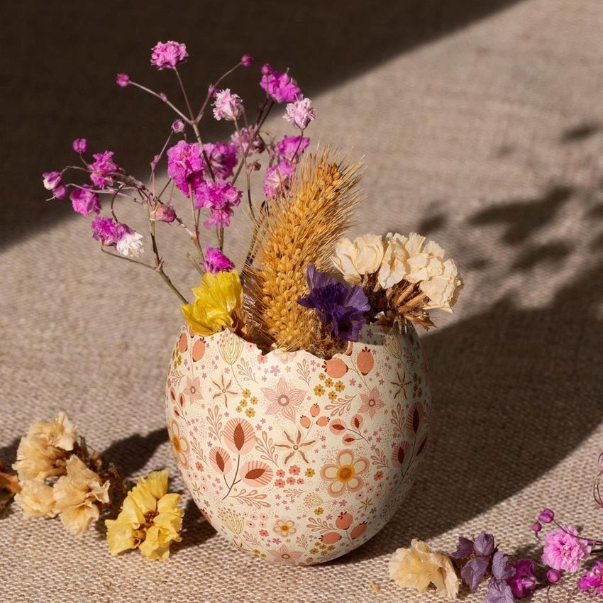 Painted Easter egg shell mockup used as a vase, holding dried flowers and wheat, placed on a textured fabric surface.