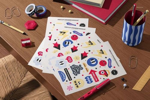 PSD mockup of kiss cut sticker sheets with playful illustrations set on a workspace with pens, tape, and paper clips.